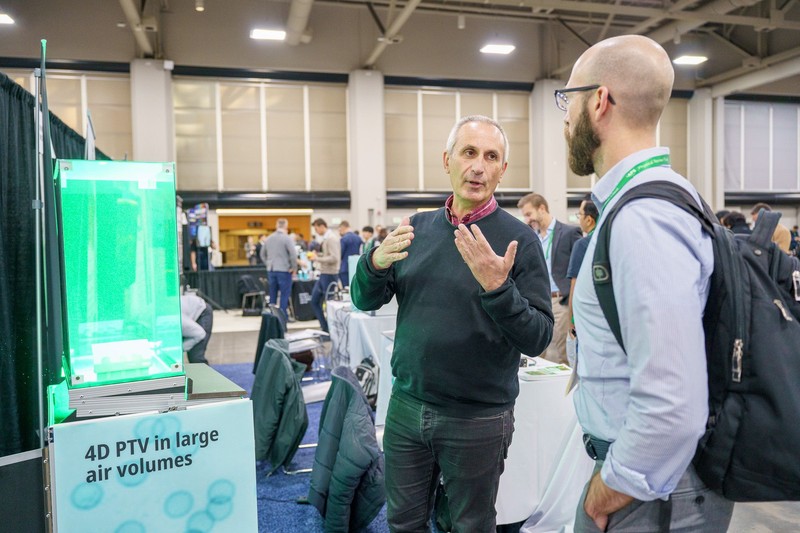 A meeting exhibitor and attendee discuss a product. 
